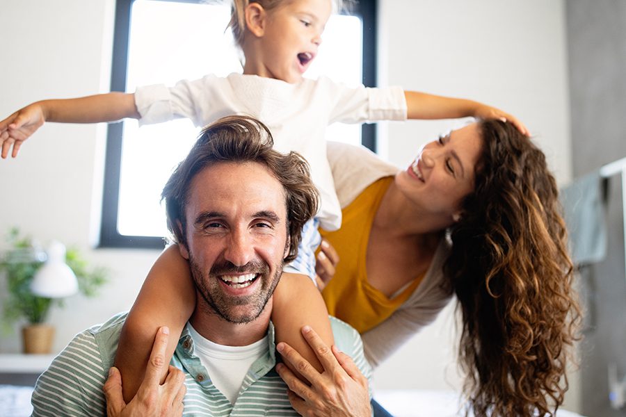 Personal Insurance - Happy Family Having Fun Time at Home With Young Girl on Her Father’s Shoulders
