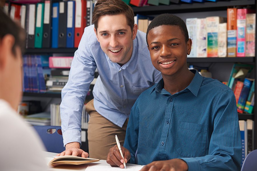 School District Employees - Teacher Helping Teenage Pupil In Class